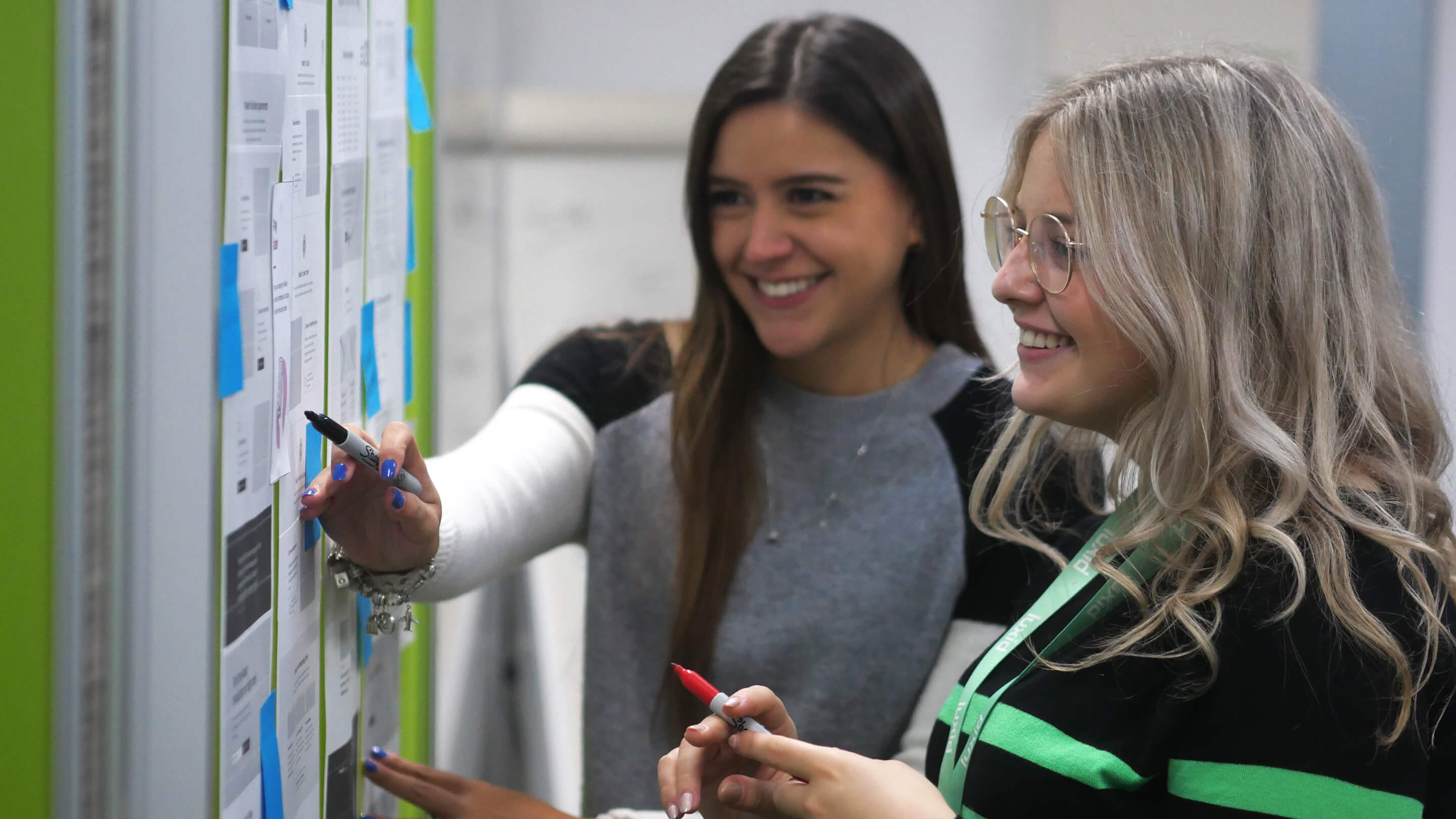 1-brunette-woman and-1-blonde-smiling-discussing-wireframes