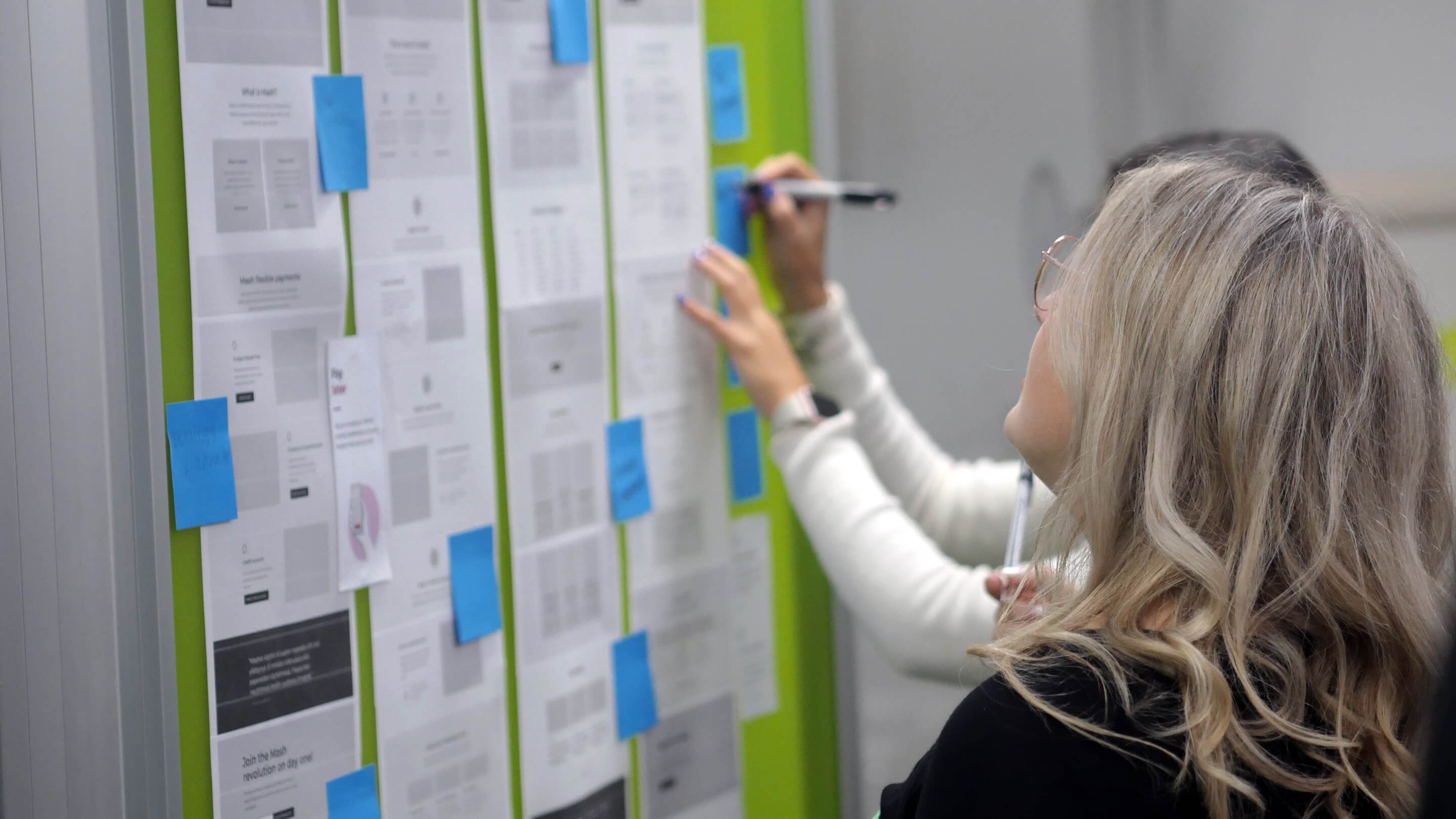 One brunette woman and one blonde woman wireframing on wall