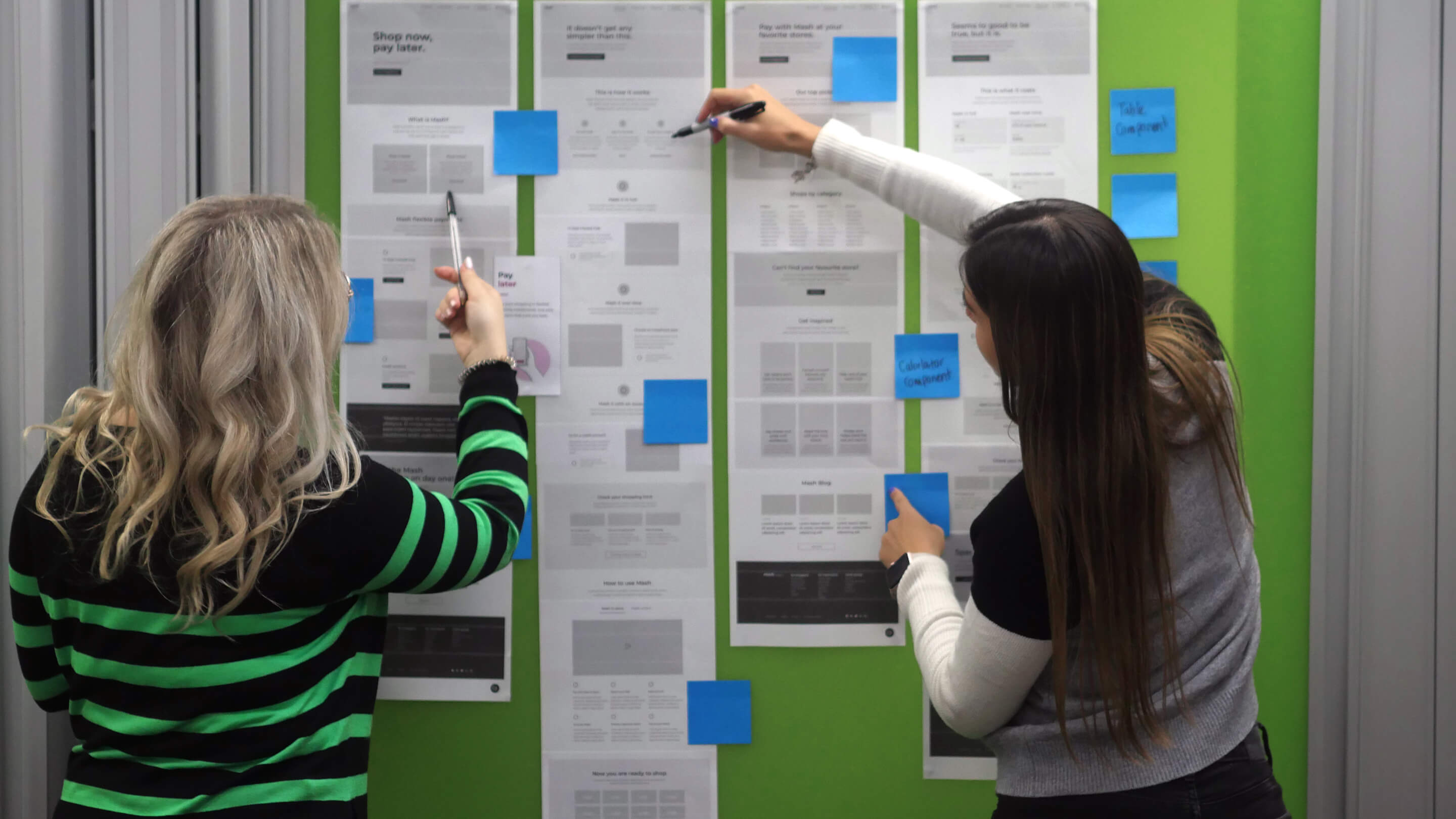 2-women-lookin-at-wireframes-on-the-wall