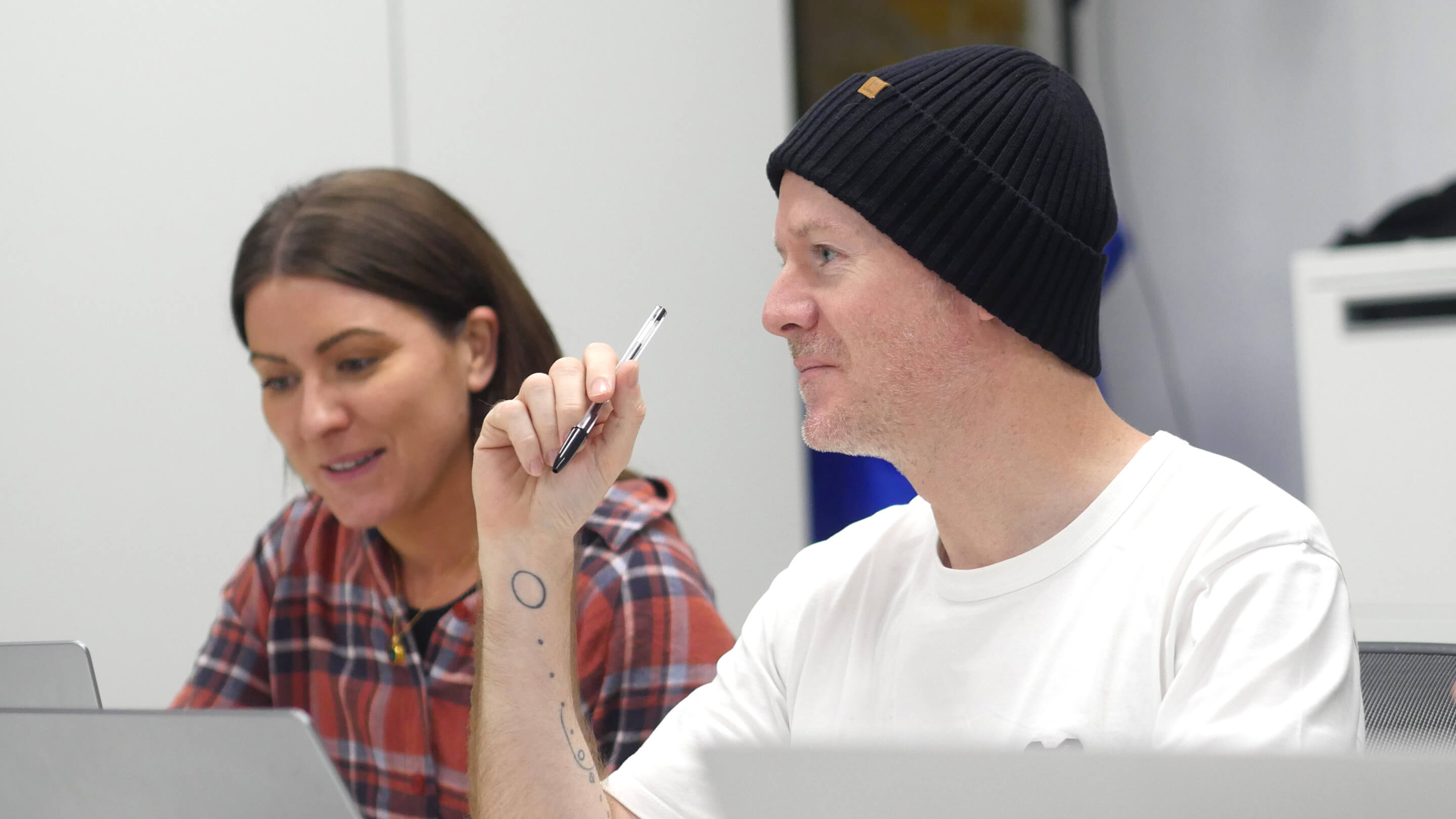 man with beanie holding pen and woman working in office meeting room