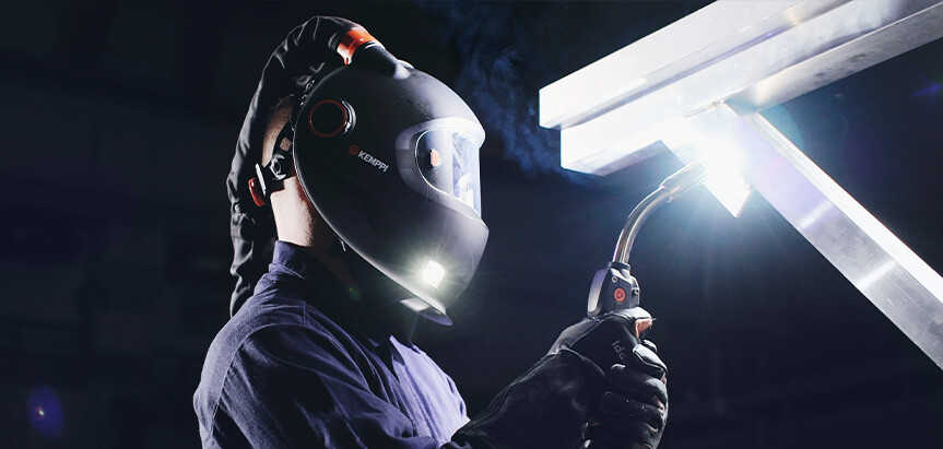 Worker wearing protective Kemppi welding helmet and gloves while welding under bright light