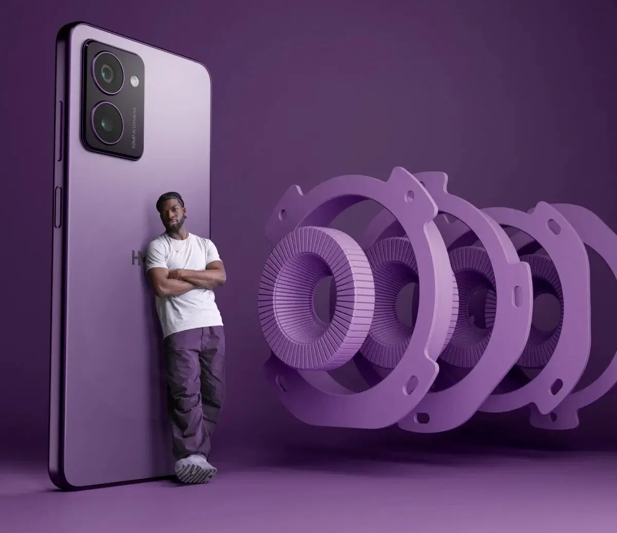 A man leaning casually against a large purple smartphone, with oversized, stylized camera lens components displayed beside it on a purple background, highlighting advanced camera technology.